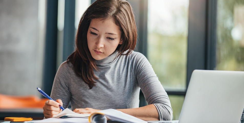 Shot of young woman taking down notes in diary. Female university student preparing note for the exam at library.