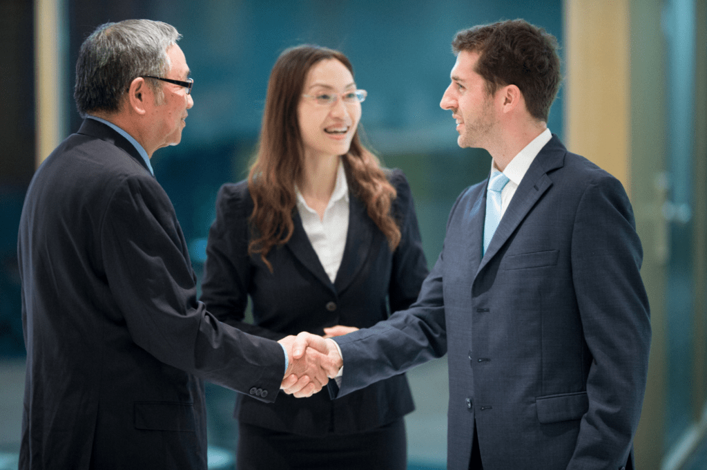 Three people in conversation. Two men shaking hands and woman speaking to one.