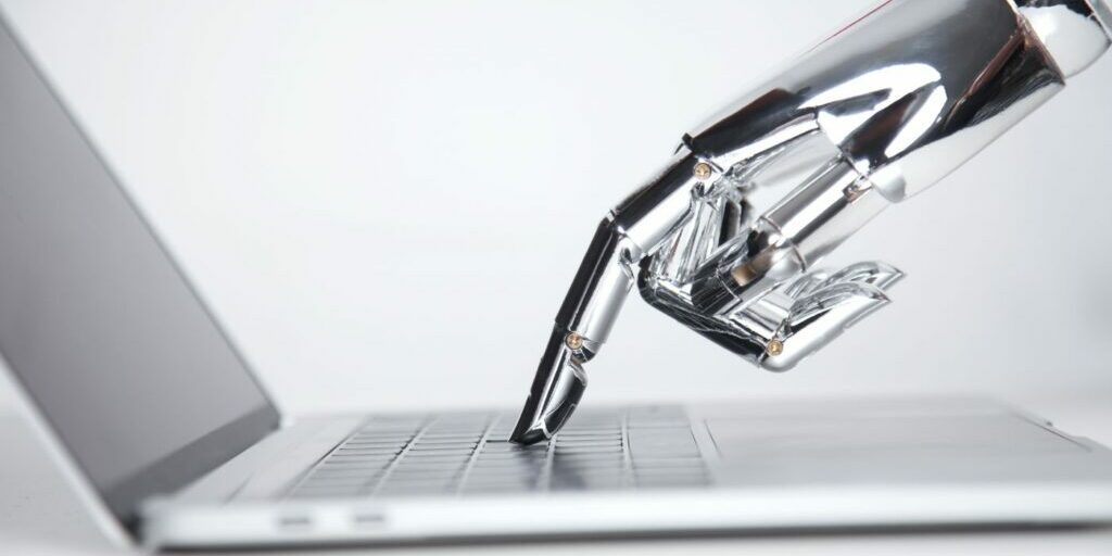 Blog banner showing a robotic hand pressing a laptop keyboard to illustrate the title "Machine Translation vs. human Translation: Will Artificial Intelligence Replace the World’s Second Oldest Profession?"