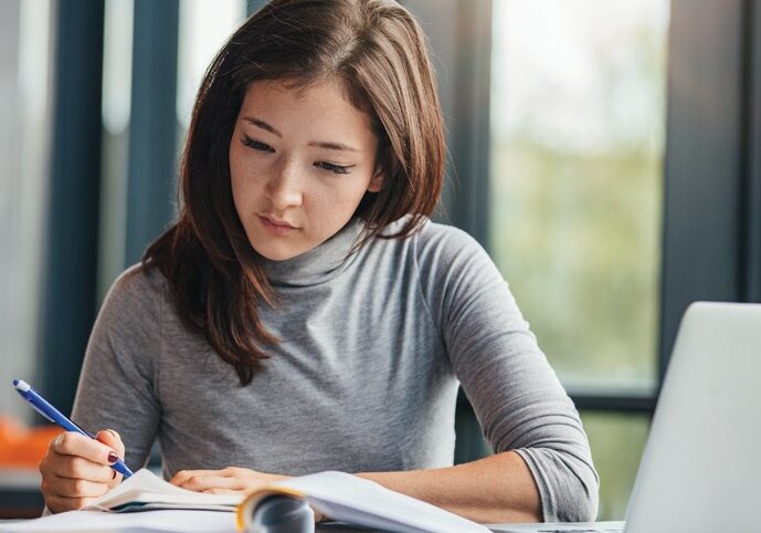 Shot of young woman taking down notes in diary. Female university student preparing note for the exam at library.