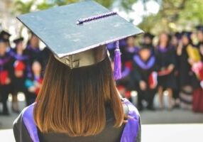 Woman standing in graduation attire facing colleagues.